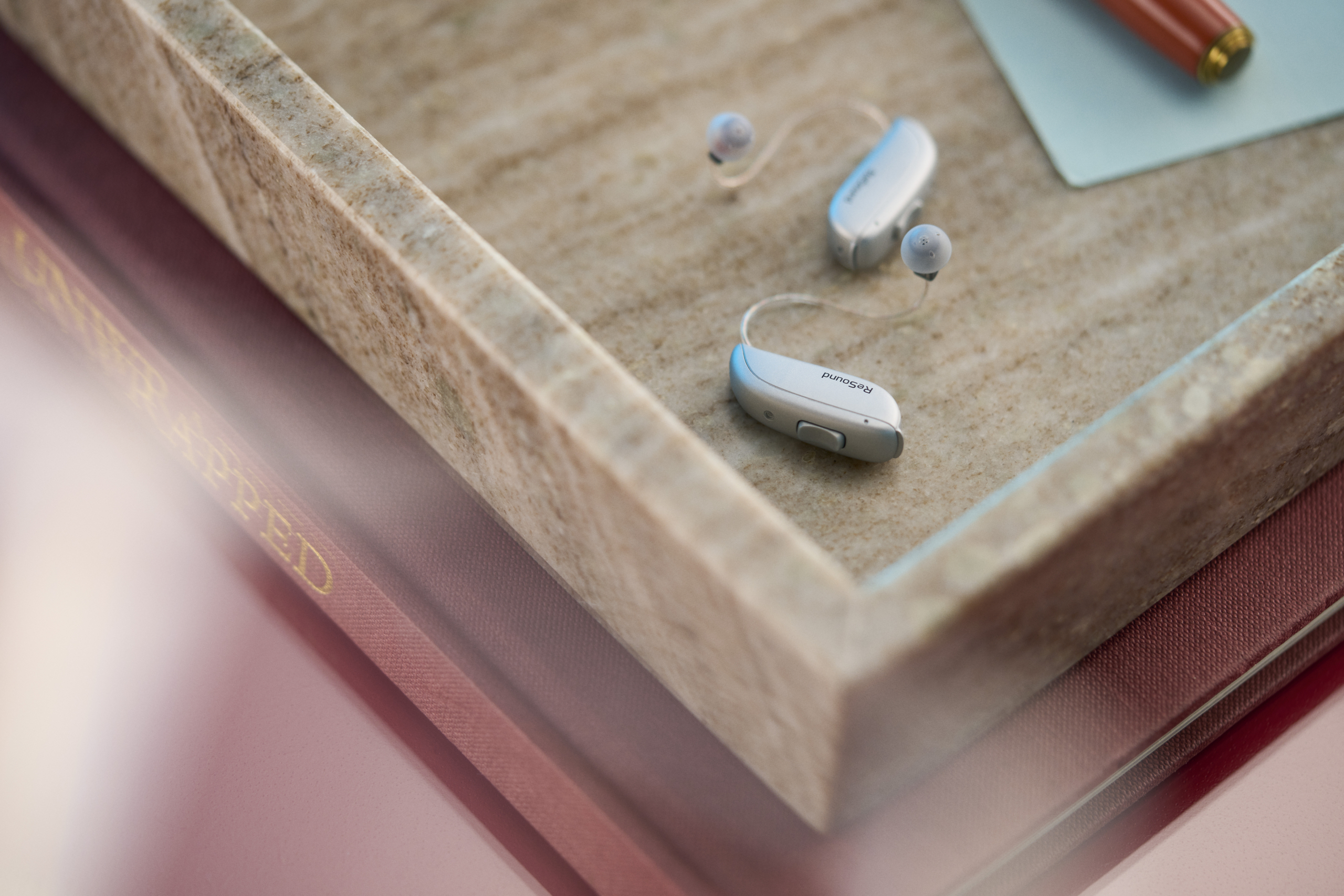 Appareils auditifs rechargeables ReSound discrets posés sur un livre, illustration du confort auditif et de la technologie moderne